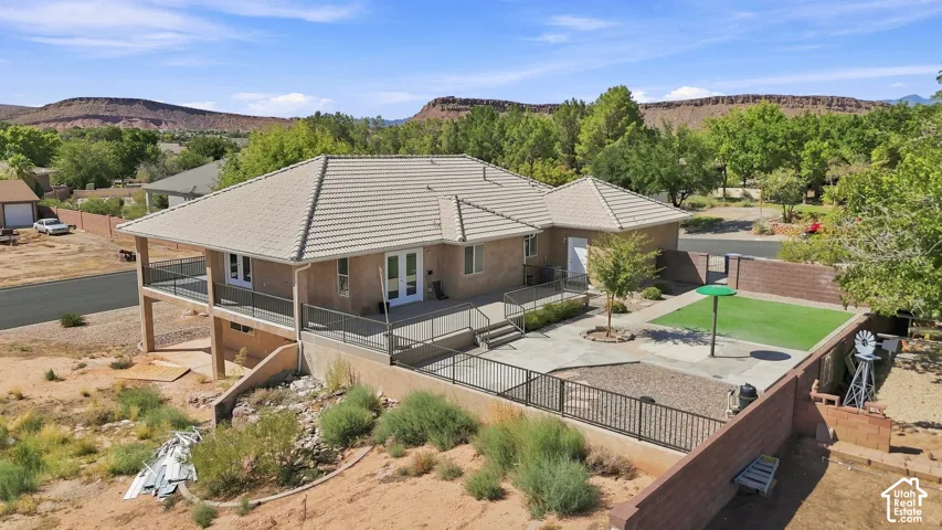 Terracotta tile roof, elevated patio with metal railing, lower-level patio, artificial turf yard section, and surrounding desert landscape