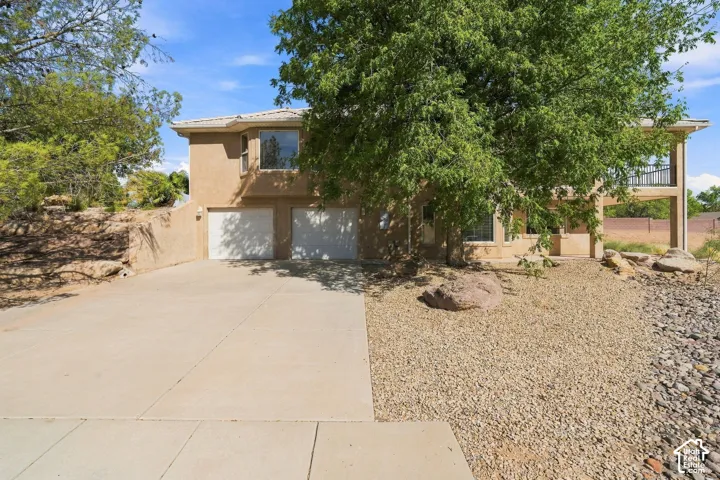 Two-car garage, stucco exterior, upper-level balcony, drought-tolerant landscaping, and mature trees