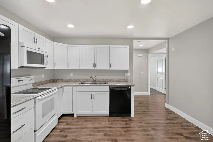 Kitchen featuring white cabinetry, light-toned countertops, stainless steel sink, wood-finish flooring, and recessed lighting