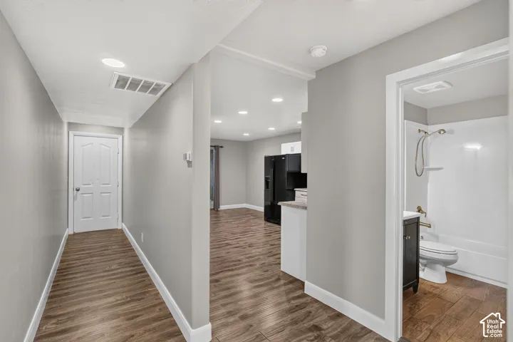 Wood-finish flooring throughout, recessed lighting, gray wall paint, white trim, and a full bathroom with a dark wood-finish vanity