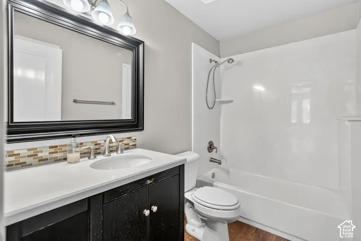 Vanity with white countertop and integrated sink, mosaic tile backsplash, framed mirror, and three-light vanity fixture