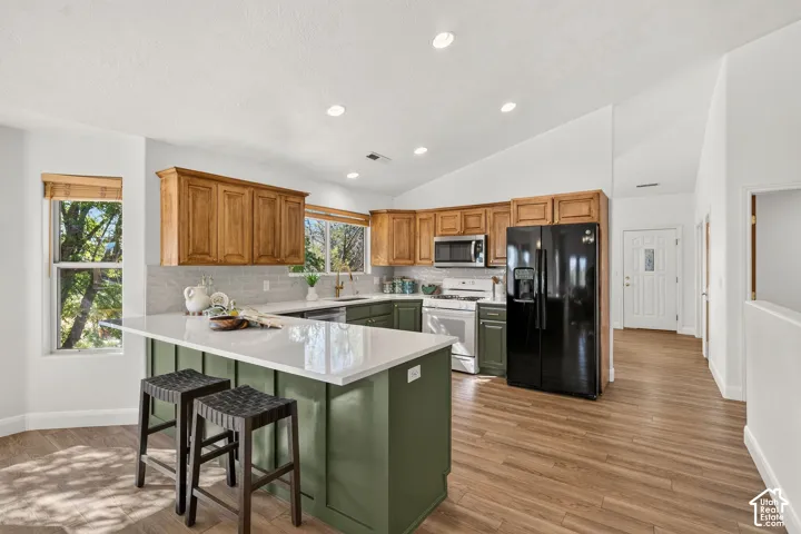 Kitchen featuring a central island with countertop seating, wood-finish flooring, recessed lighting, and vaulted ceilings