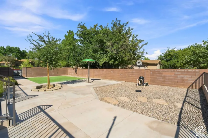 Paved patio area, stone aggregate landscaping, mature trees, and a brick privacy wall