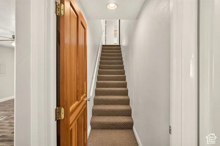Staircase with carpeted treads, white handrail, recessed lighting, and a paneled wood door