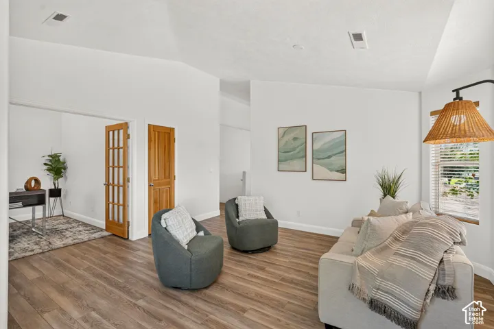 Wood-finish flooring throughout, white walls, vaulted ceiling, and French doors
