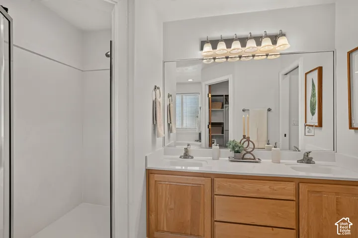 Dual sink vanity with light wood cabinetry, white countertops, and full-width mirror with an overhead light fixture