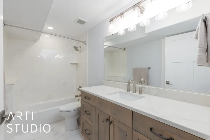 Spacious bathroom featuring a white bathtub, a vanity with a white countertop, wood-finish cabinetry, and a large wall-mounted mirror