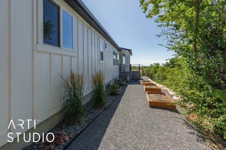 Board and batten exterior with multiple windows, gravel pathway, elevated deck, and tiered garden beds