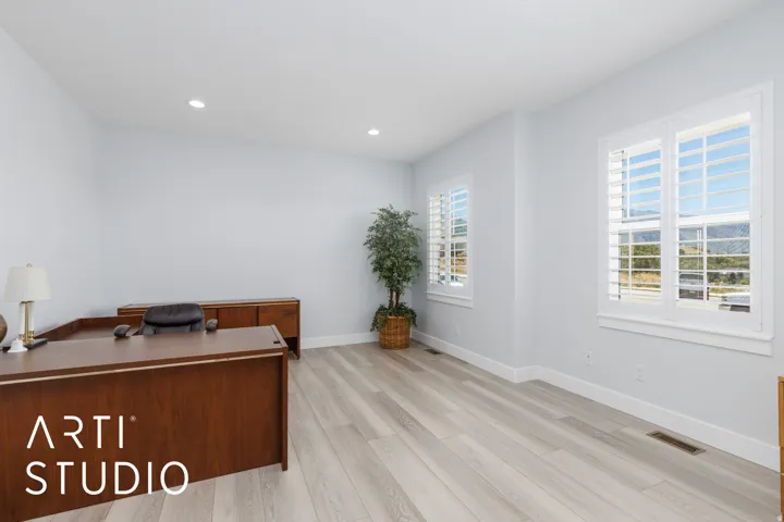 Recessed lighting illuminates the expansive room, featuring light wood-finish flooring and multiple windows with white plantation shutters