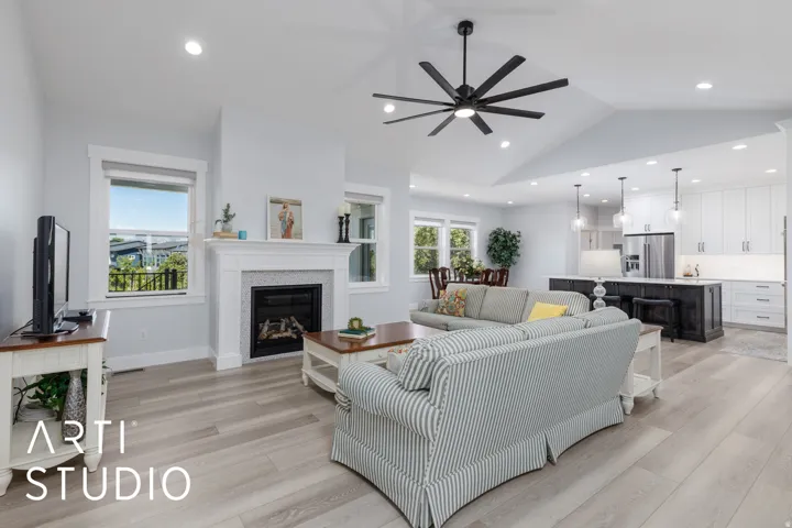 Vaulted ceilings with recessed lighting, wood-finish flooring, a built-in fireplace with a white mantel, a ceiling fan, and an open-concept kitchen with a dark-toned island