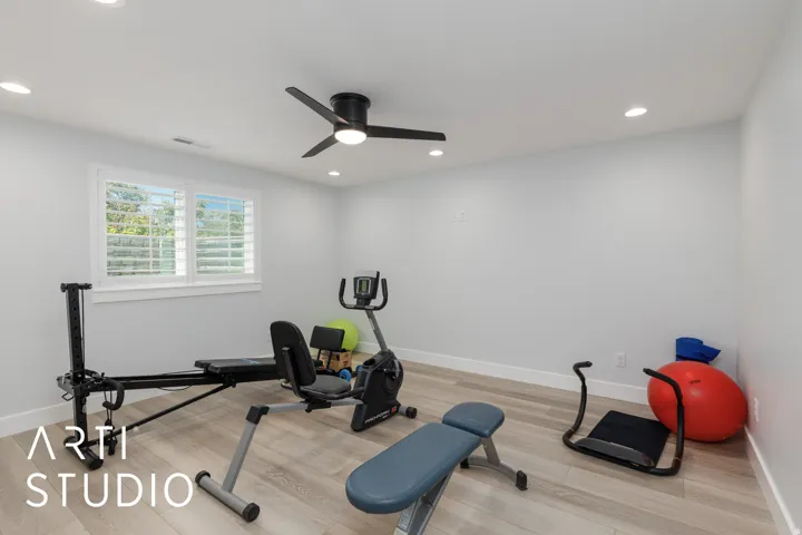 Recessed lighting, light-toned wood-finish flooring, a ceiling fan with integrated lighting, and a window with white plantation shutters