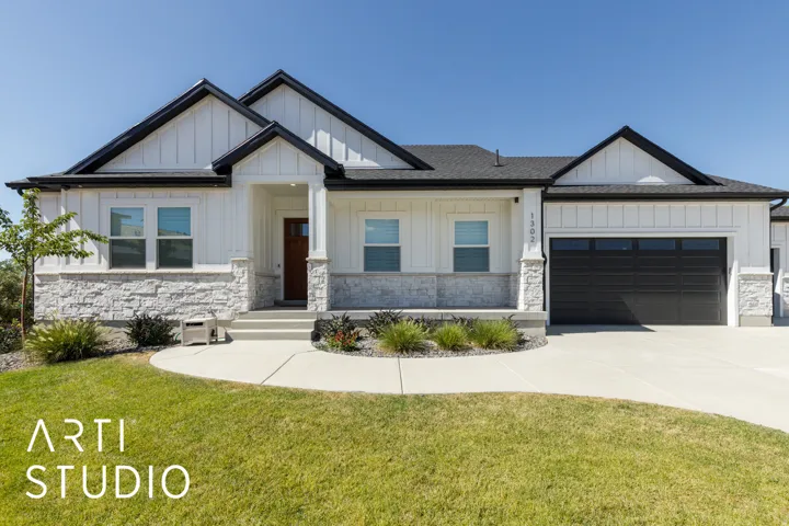 White vertical siding exterior with dark trim accents, stone facade, covered front porch, and an attached two-car garage