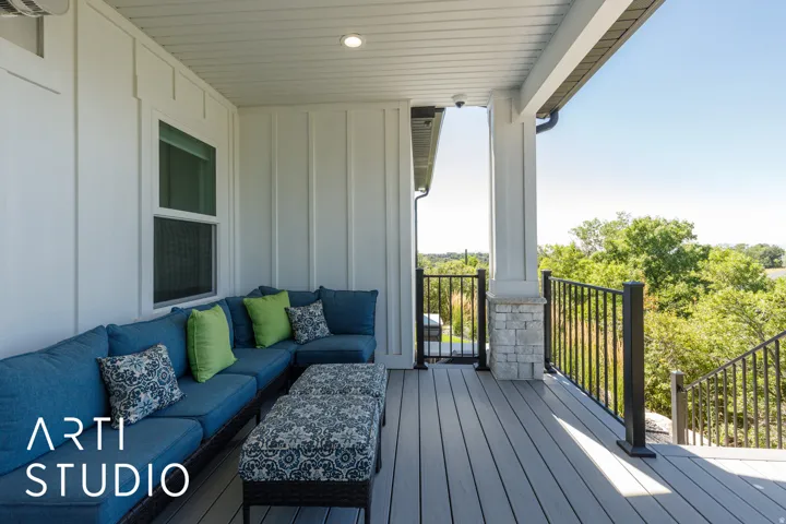 Covered deck featuring composite decking, white board and batten siding, recessed lighting, and a stone-wrapped column