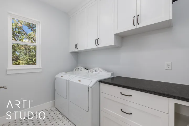 White shaker-style cabinetry, dark stone-finish countertop, and patterned floor tiling