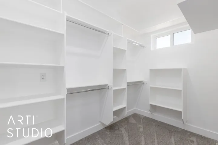 Integrated shelving and hanging rods, white walls, gray carpet, and a high-set window