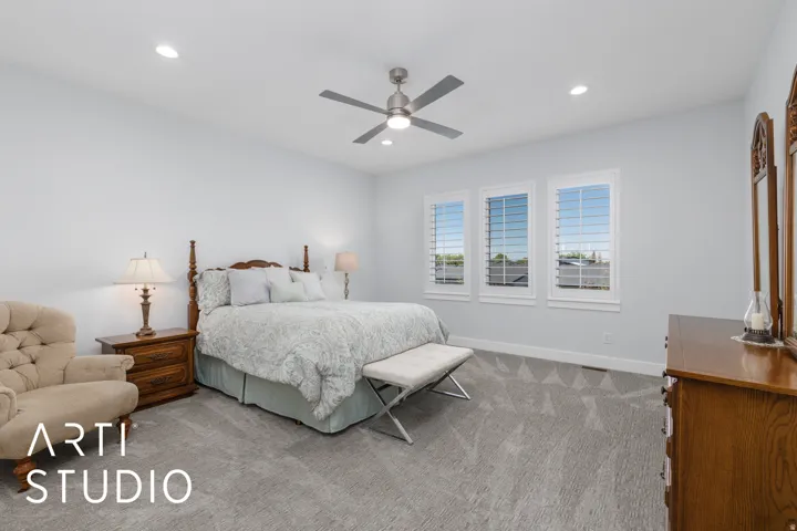 Recessed lighting, ceiling fan, three windows with plantation shutters, light gray wall paint, and patterned carpeting
