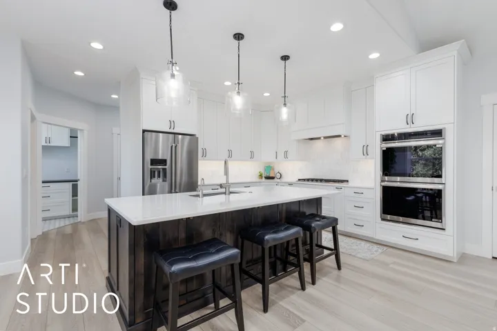 Kitchen featuring white shaker-style cabinetry, a dark wood-finish island with a light-toned countertop, stainless steel appliances, and wood-finish flooring