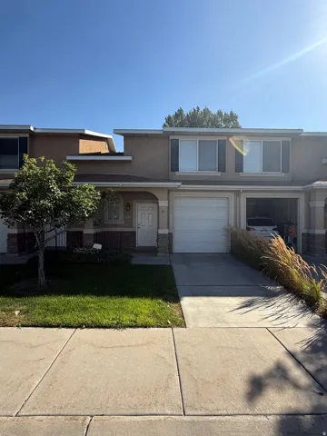 Stucco exterior with stone accent detailing, attached garage, concrete driveway, and front lawn