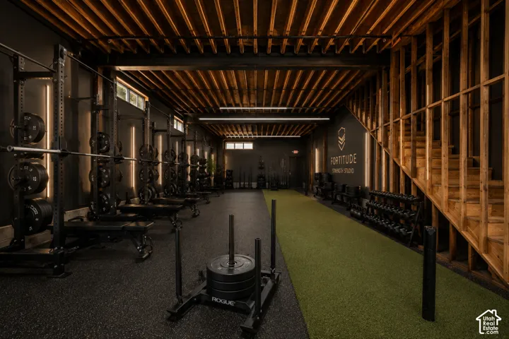 Exposed wood beam ceiling, raw wood staircase framing, multiple vertical light fixtures, rubberized flooring, and an artificial turf track