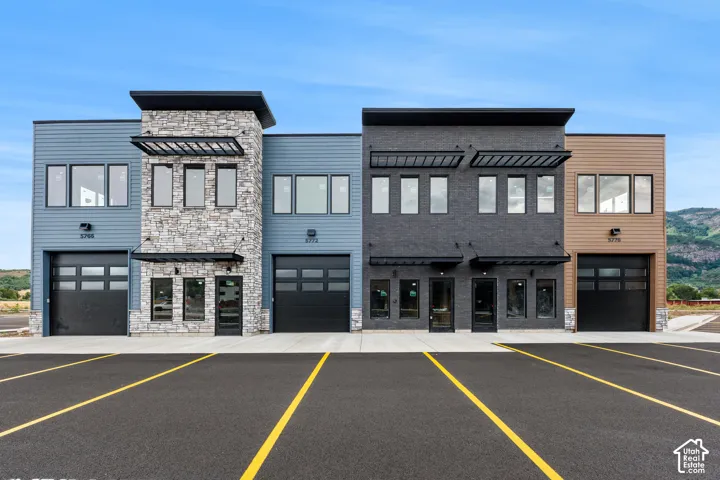 Modern building facade featuring varied siding materials, stone accents, black-framed windows, and roll-up garage doors