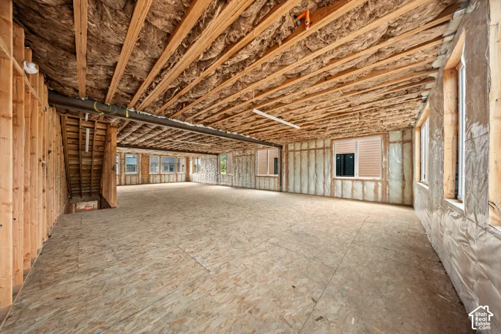 Unfinished interior space featuring exposed wood framing, ceiling joists with insulation, plywood subflooring, and multiple windows