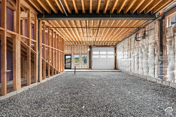 Unfinished with exposed wood framing, an overhead garage door, and a gravel floor