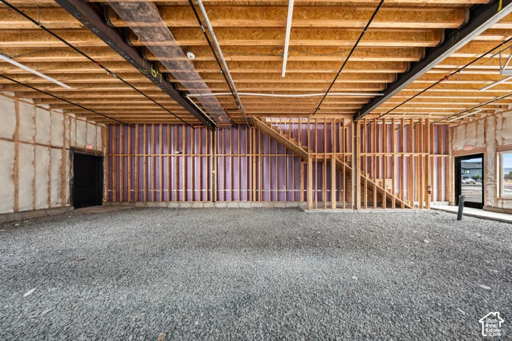 Exposed wood ceiling joists and structural beams, unfinished interior framing, insulated exterior wall, gravel flooring, and a framed staircase