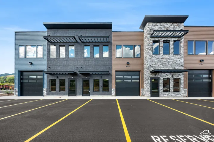 Modern facade with varied siding materials, stone accents, black frame windows, and roll-up doors