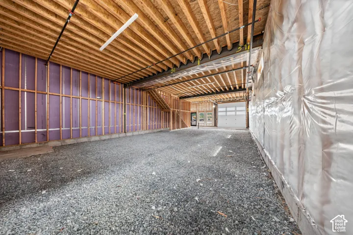 Exposed wood joist ceiling, gravel flooring, framed walls with insulation, and a white roll-up garage door