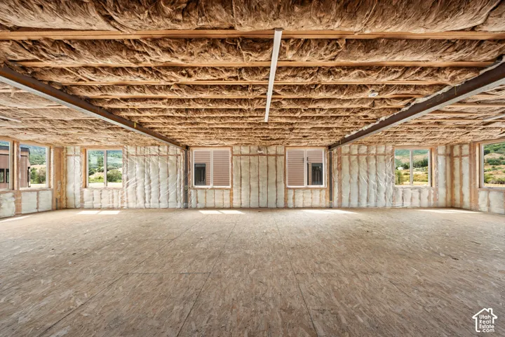 Unfinished interior space featuring exposed wood joists and insulation, multiple windows, and oriented strand board flooring