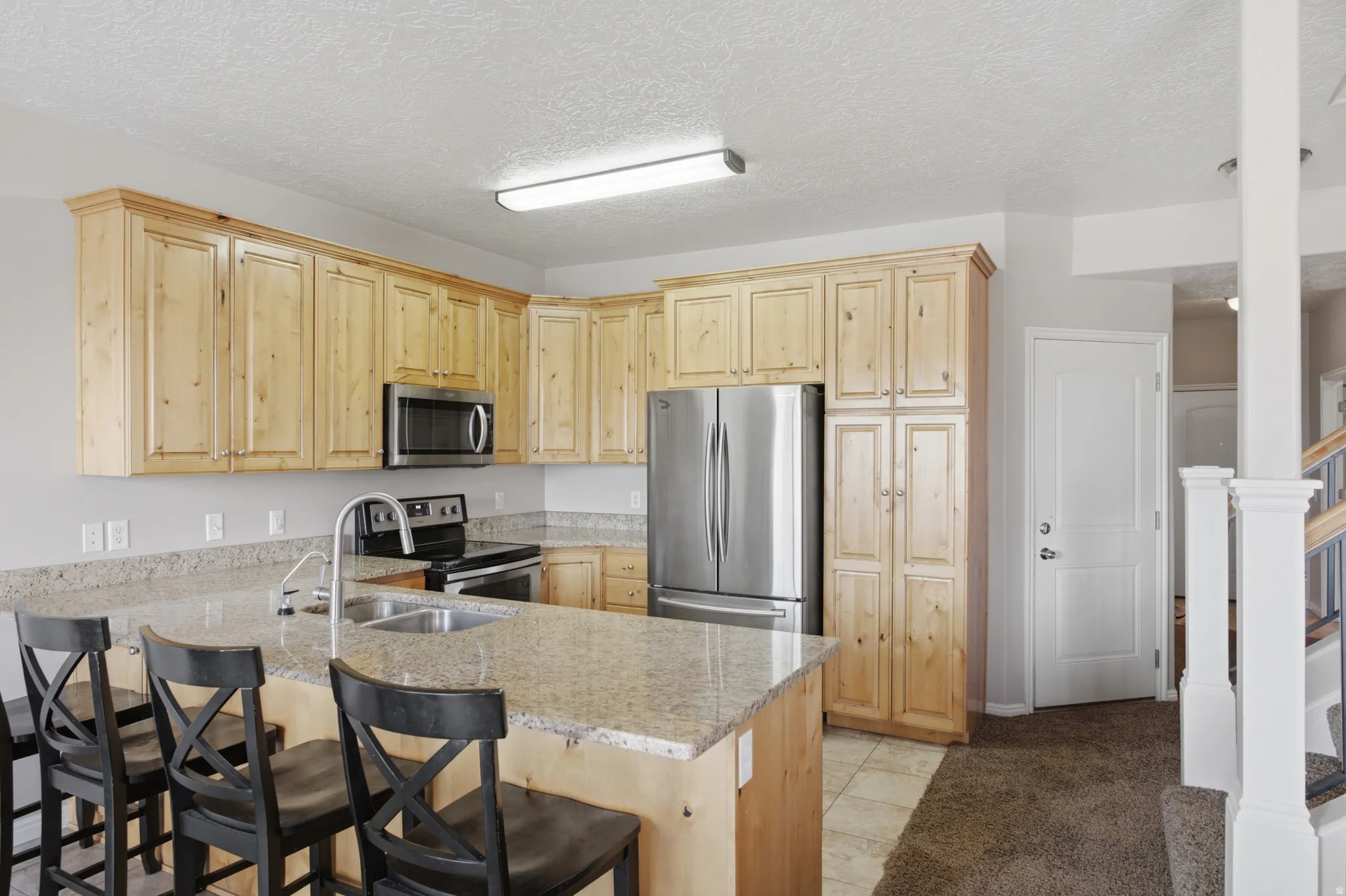 Spacious kitchen featuring natural wood cabinetry, stainless steel appliances, granite-style countertops, a large center island with seating, and recessed lighting throughout
