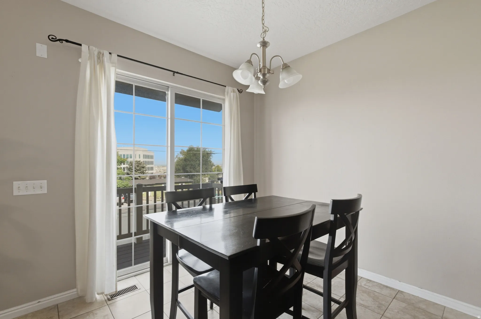 Dining area with black finish wood table and chairs, ceramic tile flooring, and dual glass doors opening to a balcony