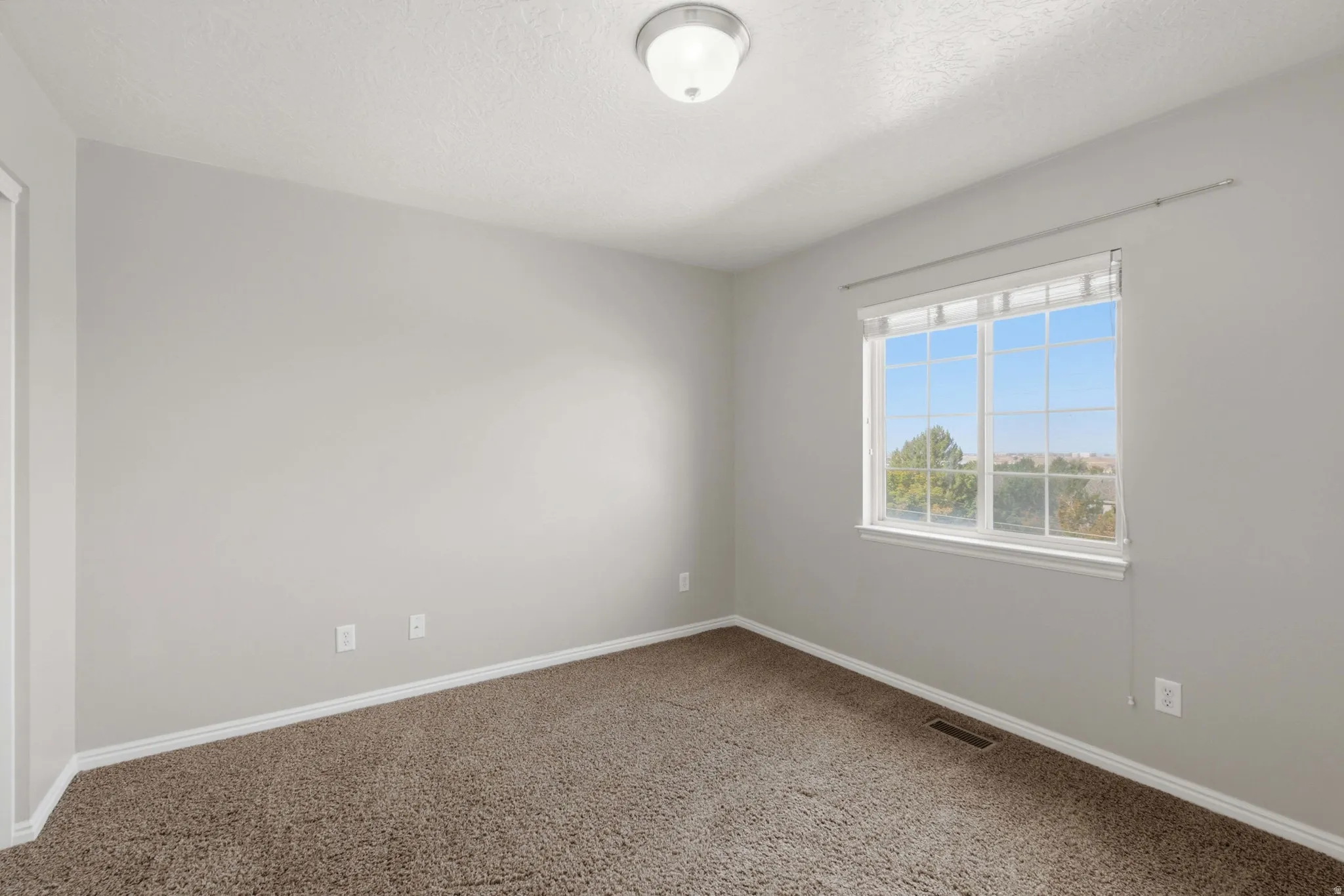 Bright and spacious bedroom offering abundant natural light through a large multi-pane window with scenic outdoor views