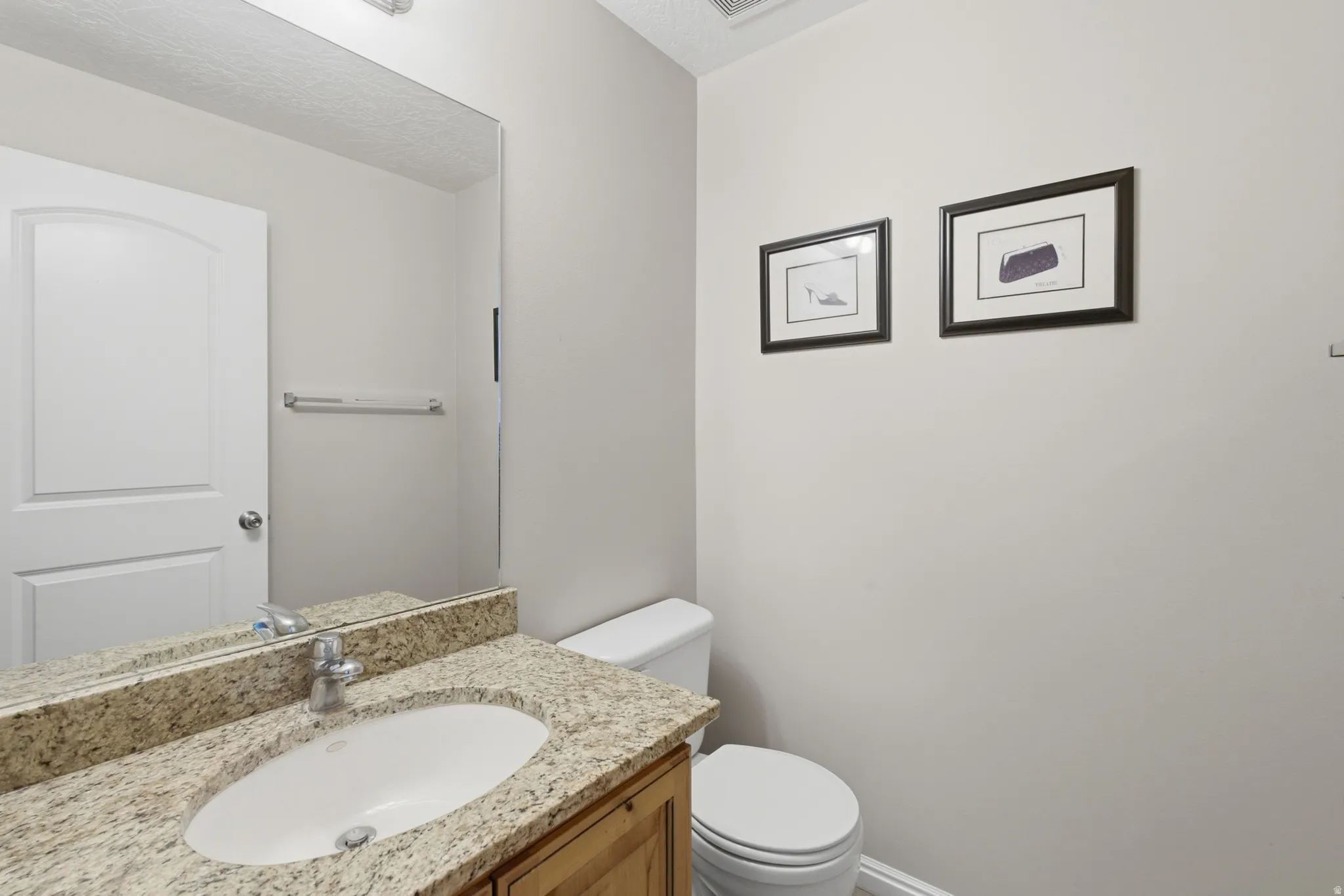 Bathroom featuring a granite-topped vanity with an undermount sink, wood-finish cabinetry, and a framed mirror