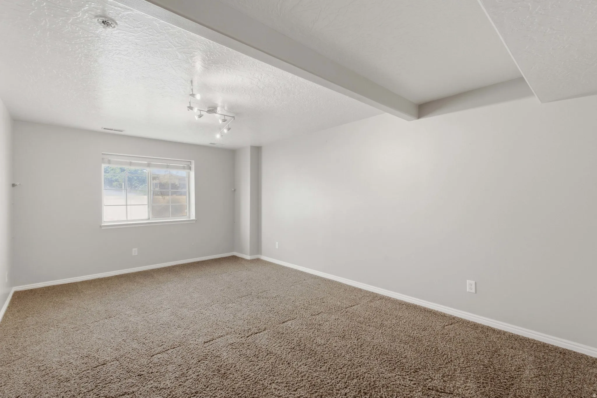Spacious carpeted bedroom featuring neutral wall finishes, abundant natural light from a large window, and recessed ceiling lighting