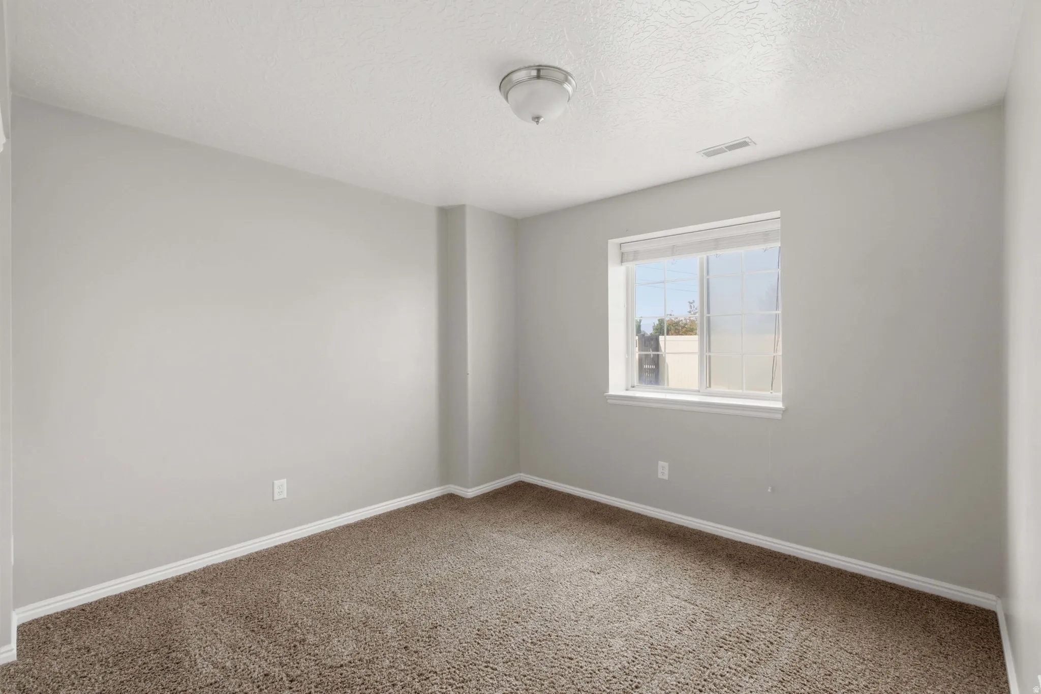 Bright secondary bedroom offering neutral walls, neutral carpet flooring, and abundant natural light from a large window overlooking the surrounding area