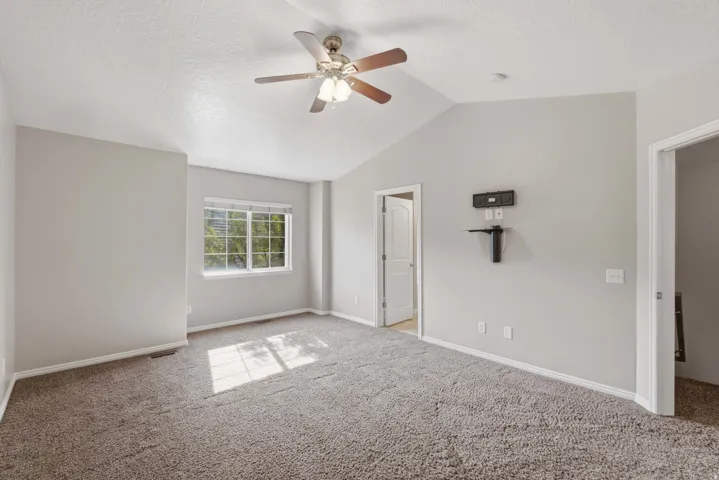 Bright primary bedroom featuring neutral wall finishes, carpeted flooring, ceiling fan with integrated lighting, and abundant natural light from dual windows