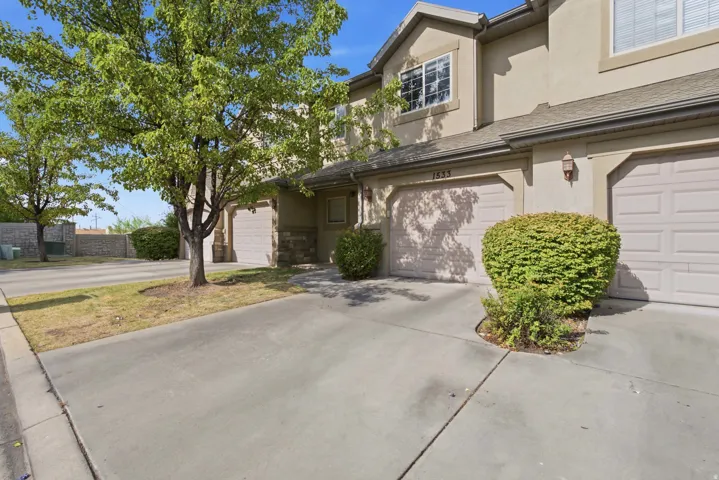 Stucco exterior with stone accents, attached garage, concrete driveway, and established landscaping