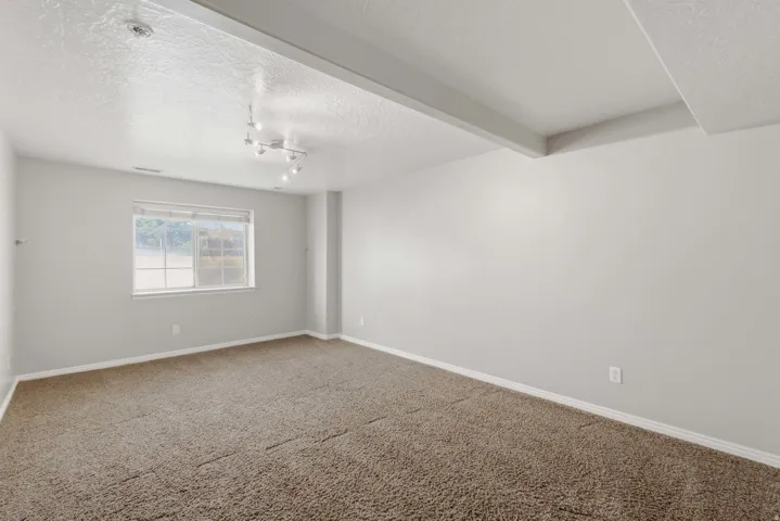 Spacious carpeted bedroom featuring neutral wall finishes, abundant natural light from a large window, and recessed ceiling lighting