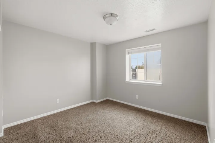 Bright secondary bedroom offering neutral walls, neutral carpet flooring, and abundant natural light from a large window overlooking the surrounding area