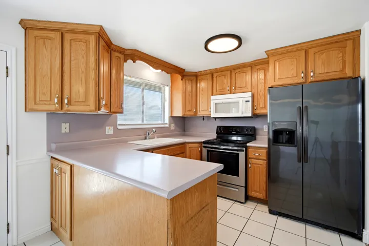 Kitchen featuring wood cabinetry, white tile flooring, stainless steel range, and a built-in microwave