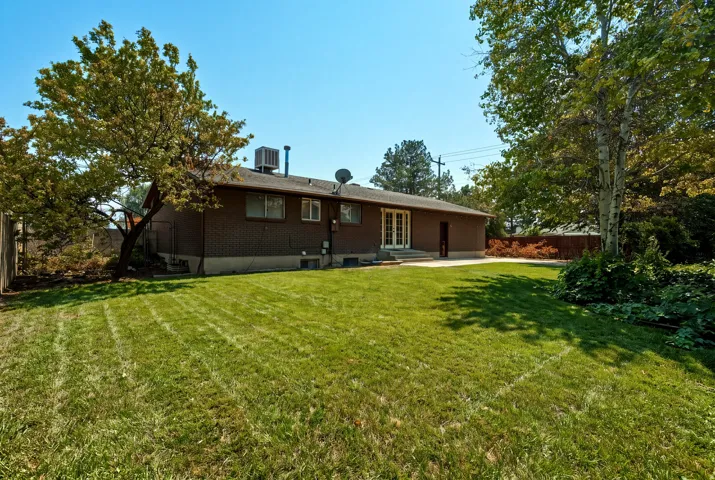 Expansive green lawn, mature trees, brick exterior, double French doors, and concrete patio