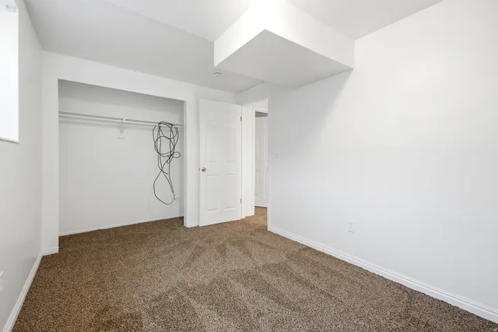Neutral color palette with white painted walls, textured carpet flooring, and a built-in closet with hanging rod