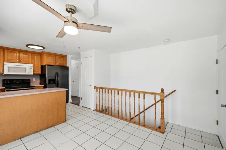 Kitchen featuring wood-finish cabinetry, black appliances, a ceiling fan with integrated lighting, and tile flooring