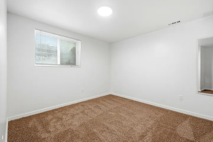 Bright interior space featuring light-colored walls, brown carpet flooring, and a window with blinds