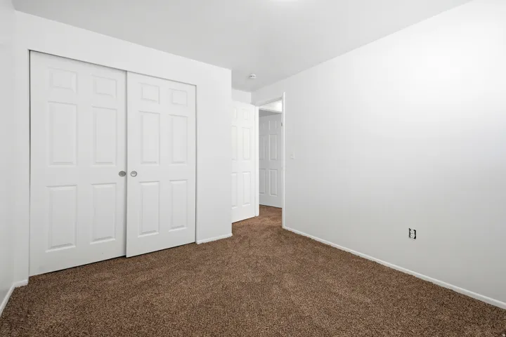 Brown carpet flooring, white painted walls, and white bi-fold closet doors