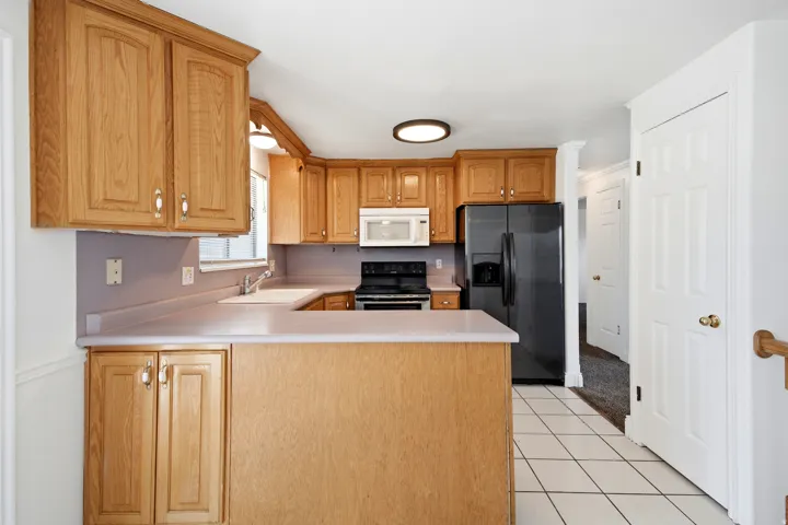 Kitchen featuring wood cabinetry, white tile flooring, and integrated black appliances