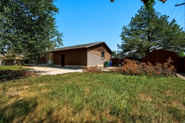Brick exterior with a concrete patio, mature trees, and a privacy fence