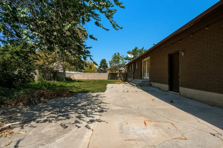 Concrete patio leading to a grass area with mature trees and a brick exterior