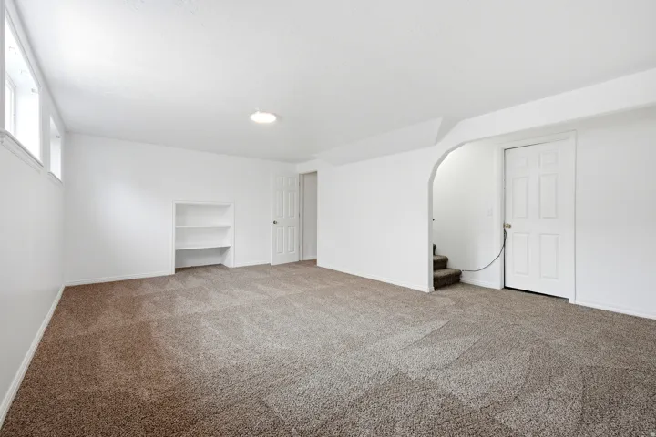 Spacious interior featuring neutral carpeting, built-in shelving, white walls, and an arched entry